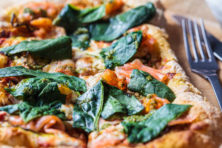 Homemade pizza with salmon, spinach, pesto and shrimps, close-up. Comfort food concept.の写真素材