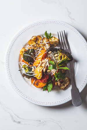 Mix of baked vegetables (broccoli, cauliflower, sweet potato and garlic) with cheese on a white plate, top view. Vegetarian healthy detox dinner.の写真素材