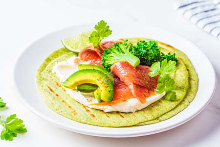 Green tortilla with broccoli, avocado, cream cheese and salted salmon on a white marble background. Vegetarian fast food.の写真素材