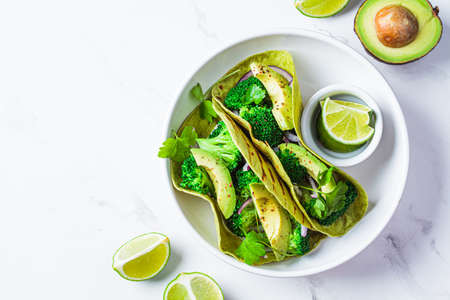 Green vegan tacos with broccoli, avocado and green flat bread in a white bowl, white marble background, top view, copy space. Vegetarian fast food.の写真素材