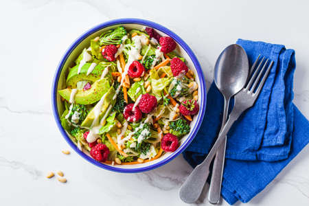 Green broccoli salad with raspberries, pine nuts, avocado and tahini dressing, top view. Vegan food concept.の写真素材