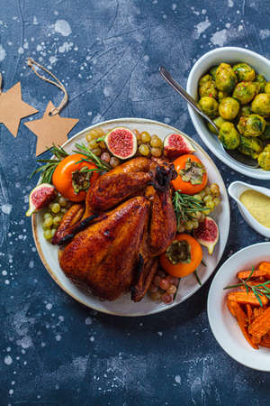 Christmas roasted whole chicken served with fruits on plate, baked Brussels sprouts and carrots on dark blue background, top view, copy space.の写真素材