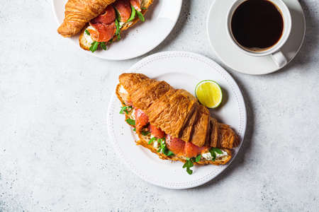 Croissant sandwich with cream cheese, salmon and arugula on a white plate, gray background, top view, copy space. Healthy breakfast concept.の写真素材