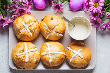 Traditional Easter cross buns with raisins on a background with flowers and colored eggs, top view.の写真素材