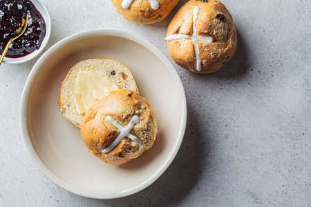 Traditional Easter cross buns with raisins, butter and berry jam on gray background, top view.