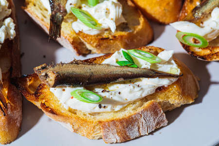 Toasts with cream cheese, fish sprats (sardine) and green onions, close-up. Simple homemade recipes...