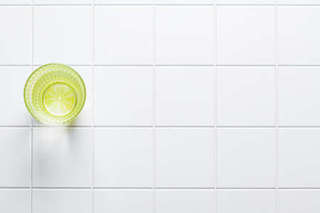 Glass of water with lime on a white tile background, copy space, top view. Water balance, healthy...