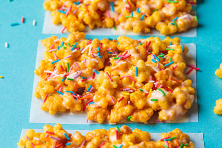 Children's corn stars cereal bars with colored sprinkles and white chocolate on a blue background.