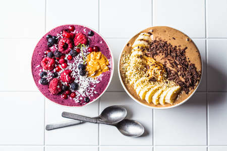 Chocolate and berry smoothie bowls on a white tile background, top view. Raw vegan food concept.の写真素材