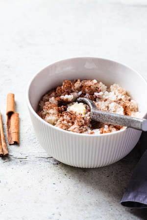 Scandinavian rice porridge with cinnamon and butter in a white bowl on a gray background. norwegian food concept.の写真素材