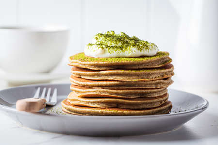 Stack of vegan pancakes with coconut cream and matcha powder on gray plate, white kitchen.の写真素材
