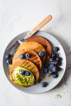 Matcha tea green pancakes with coconut cream, blueberries and maple syrup, white background, copy space. Vegan dessert concept.の写真素材
