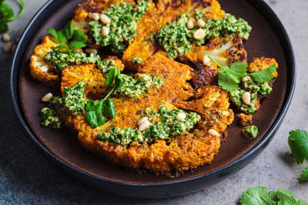 Spicy grilled cauliflower steaks with homemade green pesto on dark plate, dark background.の写真素材