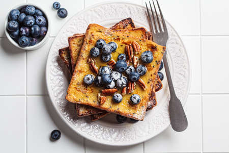 French toast with blueberry, pecan and maple syrup for breakfast on white plate, top view.