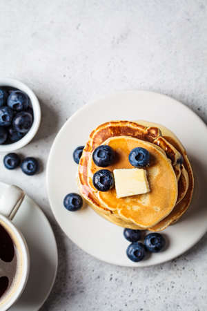 Stack of blueberry pancakes with maple syrup and butter on a white breakfast plate, top view.