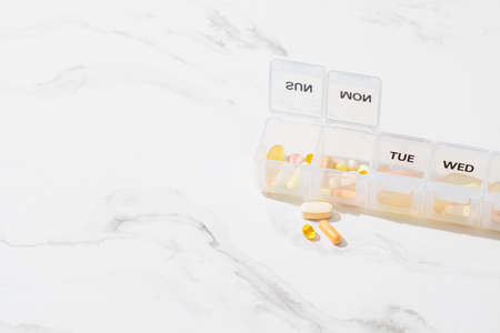Pills box for daily intake of vitamins and medicines. Various capsules and tablets in a white...
