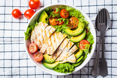 Grilled chicken breast salad with avocado and cherry tomatoes in white bowl, top view. Healthy diet food concept.の写真素材