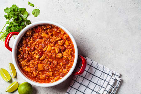 Vegan chili con carne with vegetables and beans in tomato sauce in red saucepan, top view. mexican...