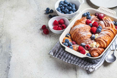 Croissant baked french toast with cream cheese and berries in a dark oven dish, copy space. Delicious breakfast recipe concept.の写真素材