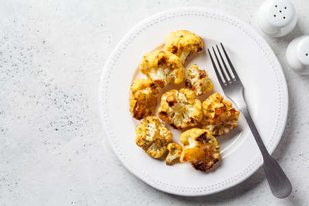 Baked crispy spicy cauliflower on white plate, top view. Cooking healthy vegan food concept.の写真素材