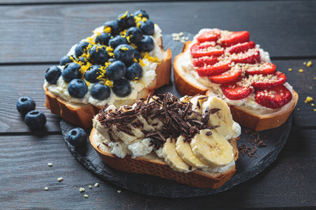 Fruity vegetarian toasts for breakfast on dark wooden background. Bread slices with ricotta, berries, banana, chocolate and seeds.の写真素材