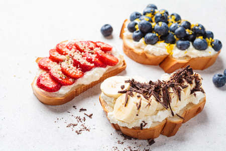 Fruity vegetarian toasts for breakfast on gray background, copy space. Bread slices with ricotta, berries, banana, chocolate and seeds.の写真素材
