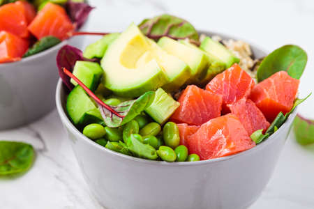 Healthy version of Hawaiian poke - brown rice, salmon, edamame, cucumber and avocado in a gray bowl,...