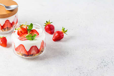 Strawberry parfait with yogurt and granola in a glass jar, copy space. Healthy breakfast recipe. Summer dessert concept.