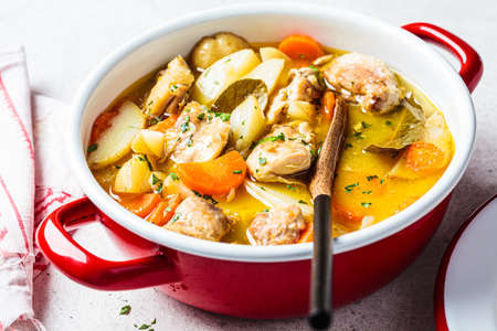 Chicken stew with potatoes and carrots in red pot. Chicken soup with vegetables and herbs. Comfort food recipe.の写真素材