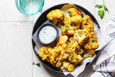 Baked spicy cauliflower wings with yogurt sauce in a black plate, top view. Vegan diet recipe concept.の写真素材