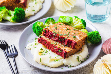 Lentil meatloaf pieces with mashed potatoes and broccoli on a gray plate, close-up. Vegan christmas recipe.の写真素材