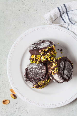 Chocolate cookie ice cream sandwiches covered with dark chocolate and pistachios on plate, top view.の写真素材