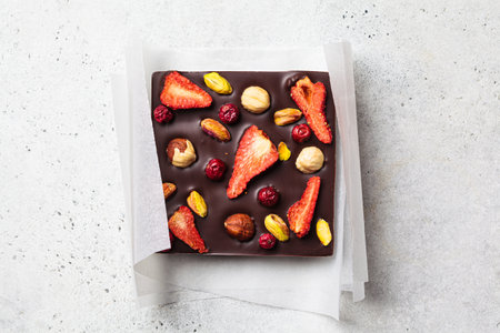 Bar of homemade dark chocolate with berries and nuts on white paper, top view.の写真素材