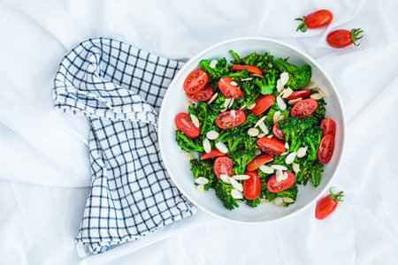Broccoli salad with cherry tomatoes and almonds in a white bowl, top view. Vegan detox recipe.の写真素材