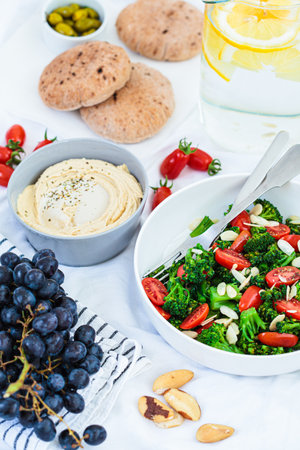 Vegan picnic food: hummus, lemonade, broccoli salad and fruits on a white blanket on the grass.の写真素材