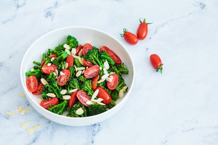 Broccoli salad with cherry tomatoes and almonds in a white bowl. Vegan detox recipe.の写真素材