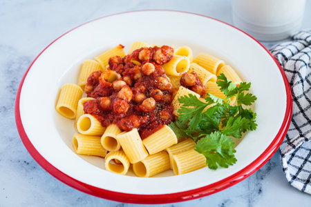 Vegan rigatoni pasta with chickpeas and tomato sauce in white plate, top view. Italian food concept.の写真素材