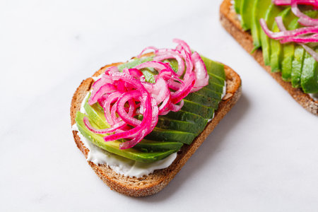 Avocado toast with cream cheese and pickled onions on a white plate.の写真素材