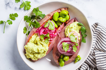 Baked sweet potato halves with guacamole, edamame beans, pickled red onion and cilantro, top view....