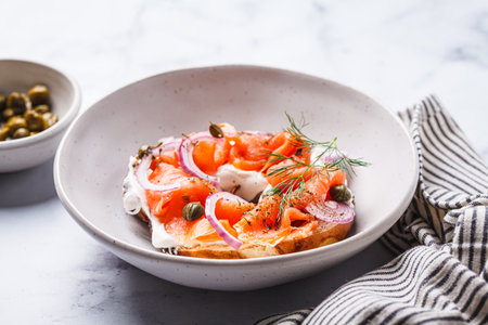 Breakfast bagel with salmon, cream cheese, capers and onions, white marble background.