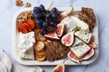 Assortment of cheeses and fruits platter with wine, on white marble table, top view.