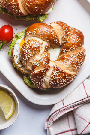Breakfast bagel with egg and avocado guacamole on a white plate, top view.