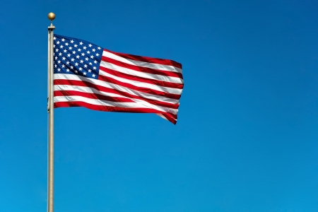 US American flag waving in the wind with beautiful blue sky in background