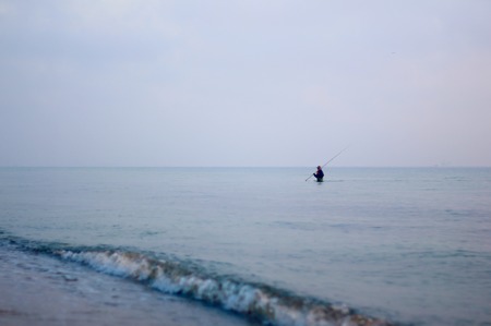 Fisherman in the sea by the beach early in the morning. Minimalism wide shot. Blue and grey colors. Tunisia - Monastir Skanesの写真素材