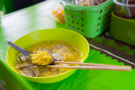 yollow asina style noodle call ba mee with meat ball on spoon and chopstick on green resterant table...