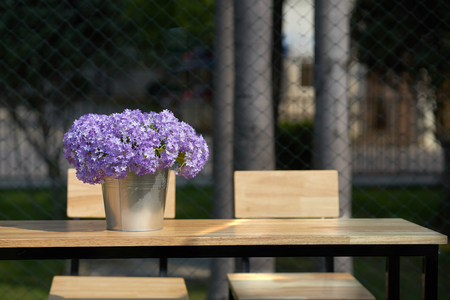 purple flowers in bucket vase on wooden table with chairs with sunlight and shadeの写真素材