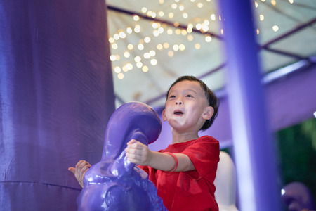 boy ride on purple horse,carousel or merry go around or roundabout with blur bokeh light on backgroundの写真素材