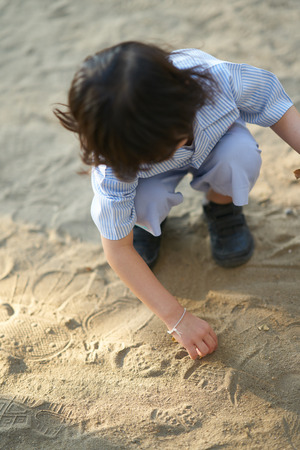 Kid in uniform student kindergarten school sit and play on sand or soil floor in playground with sun light in the morningの写真素材