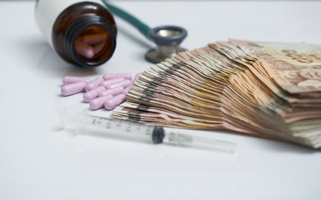 Money banknote and purple capsules  in moddle surround by blur jar,syringe and stethoscope on white background in important money saving for health care or insurance conceptの写真素材