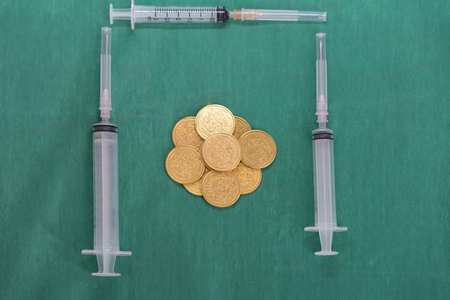 Coins or money with multiple syringes on surgery green dress cover background in health ,surgery ,treatment -cost conceptの写真素材